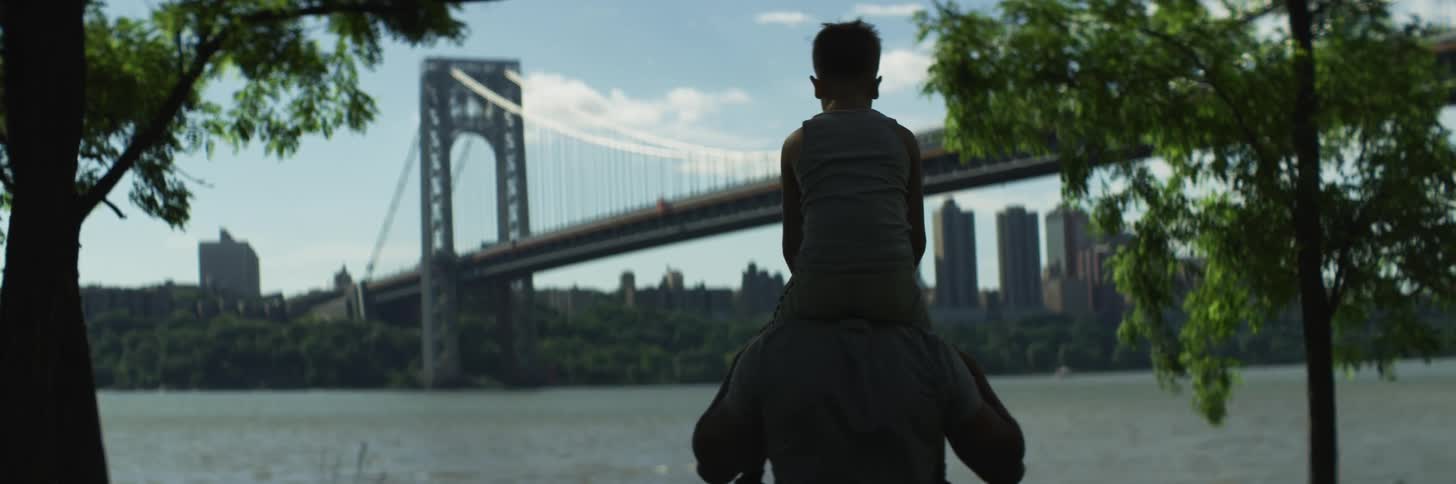 A man standing on the shore lifts his son up on to his shoulders