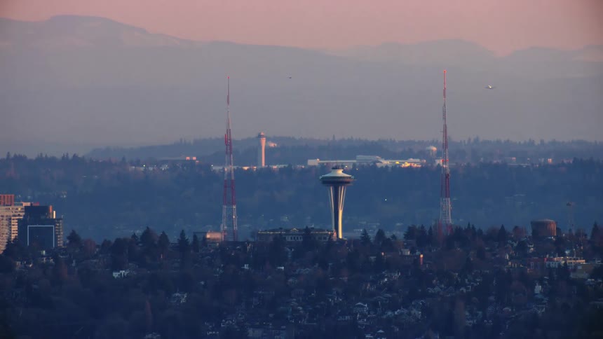 Two large radio antennae from the Space Needle as a large jetliner takes off in the background in this aerial of downtown Seattle at sunset on a clear evening
