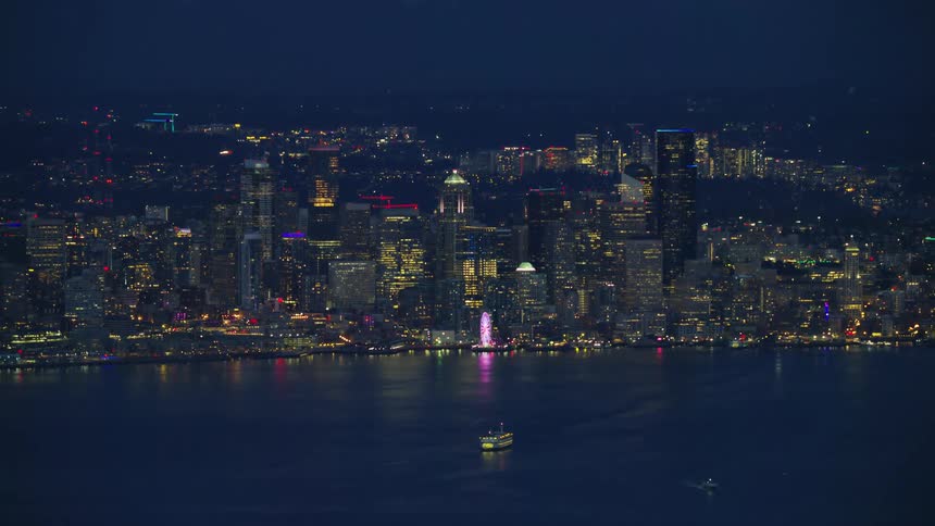 Slow zoom out reveal from the Great Seattle Wheel to the whole city and Puget Sound when the city of Seattle is illuminated by awesome evening lights