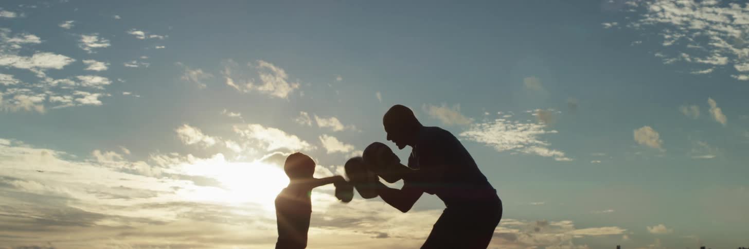 Man coaches young kickboxer backlit by sun