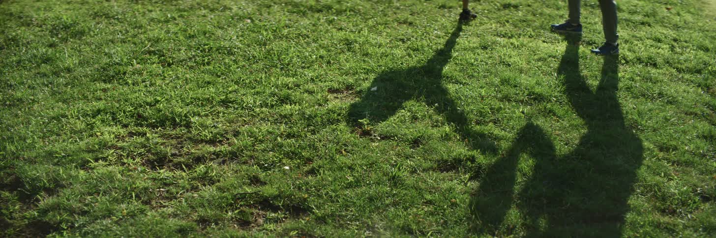Shadows cast by boy and his kickboxing trainer can be seen against lawn