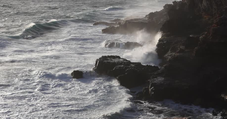 Waves crash against black rocky shore sending spray into the air