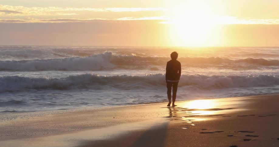 A person walking on a beach with sand and waves with the sky and clouds in the background