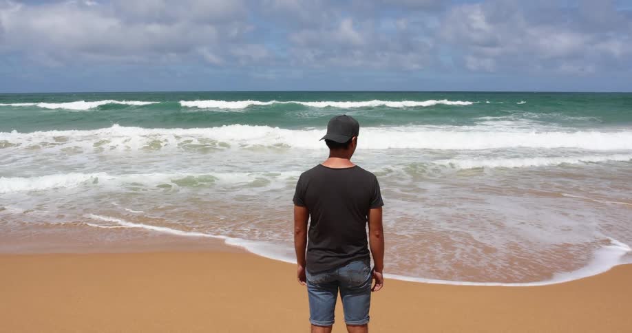 Man standing on the sand beach next to the ocean at daytime