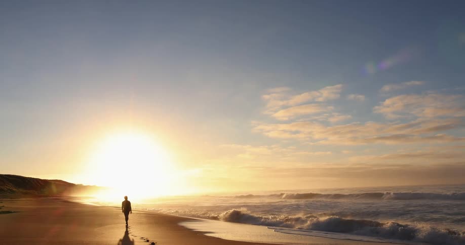 Silhouette of a person walking on the sand beach at sunset