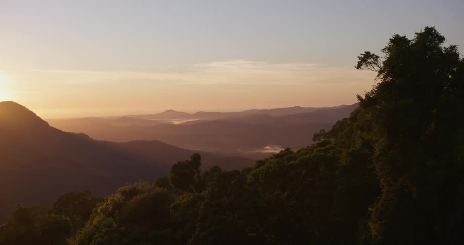 A landscape with trees in the foreground with a mountain range the sky and clouds in the background