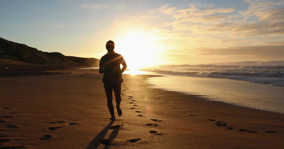 A man runs on the beach along the coast as the sun rises over the horizon