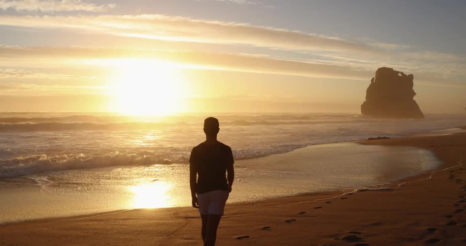 A man is walking on the beach at sunrise
