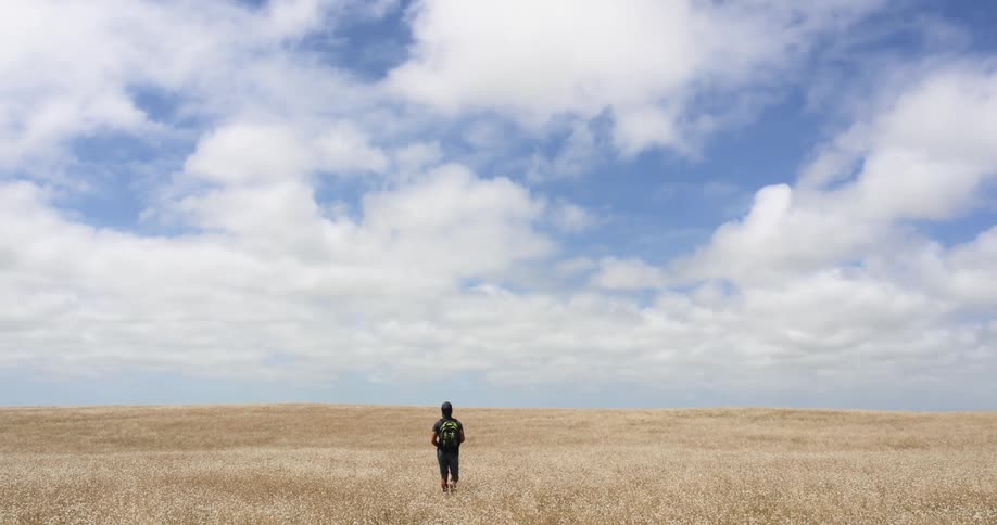 Man wearing a backpack walking on the dry yellow grass on a prairie in the countryside