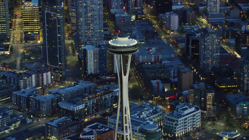 Aerial view of the Space Needle Spire at the Seattle Center as the camera flies around the needle showing downtown city streets