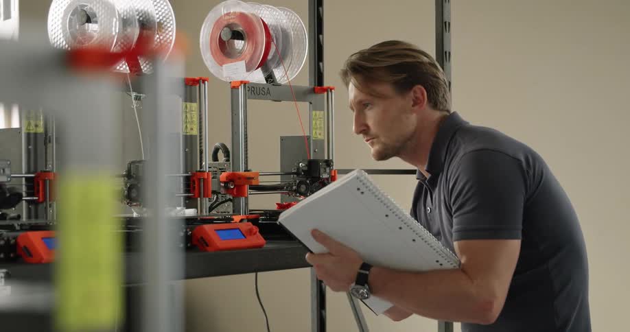 A man looks closely at some equipment and takes notes on how it is functioning