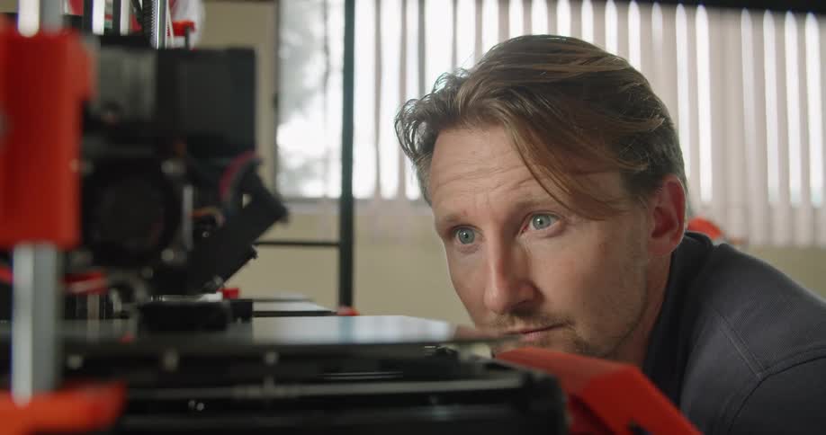 A man in an office bending down to watch a machine as it works