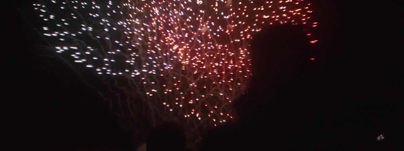 A pair of silhouettes look up at the night sky as colorful fireworks burst overhead