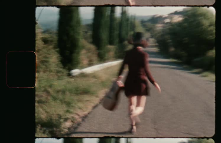 A woman carrying a guitar runs down a street