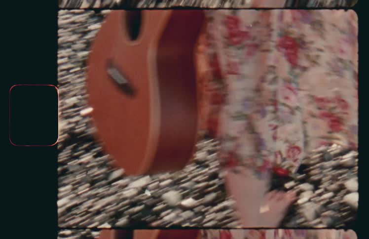 A woman carrying a guitar walks barefoot on rocks