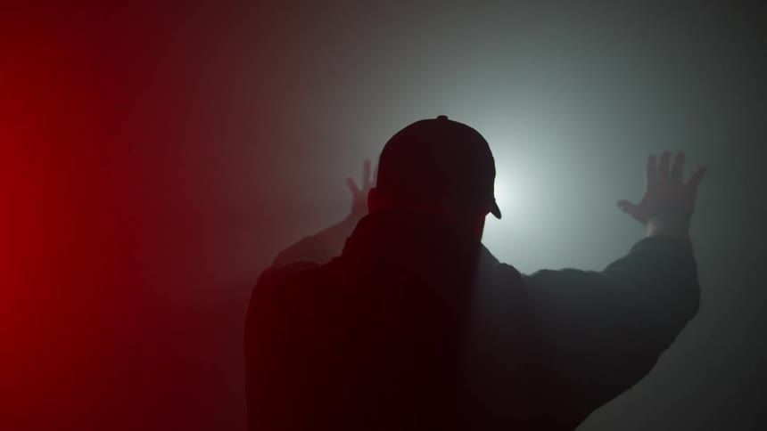 Bearded man wearing a baseball hat with hands extended towards white light