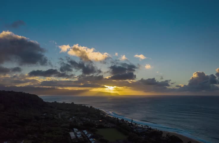 Waves roll in on coast as the sun sets and clouds move across the sky