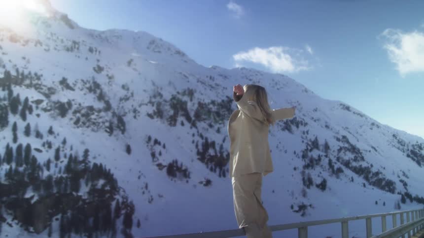A woman standing by a road with a snow covered mountain range the sky and clouds in the background