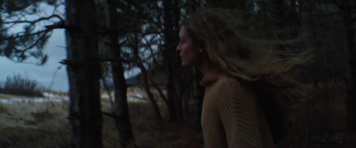 A woman with a sweater walking in the forest with the sky and clouds in the background