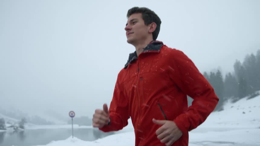 A man jogging next to a lake during a snowstorm in winter