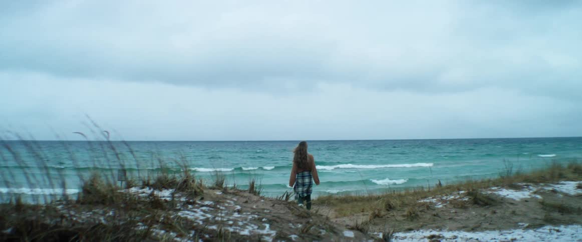 A woman walking alone on a beach on a cloudy windy day