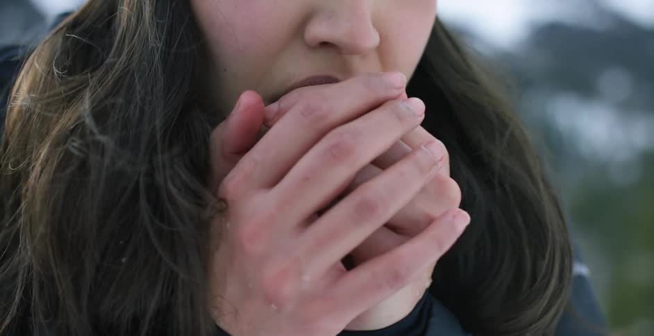 A woman shivers and blows on her hands to keep warm while outdoors