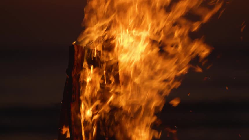 Tall pieces of wood held together vertically burn outside at night