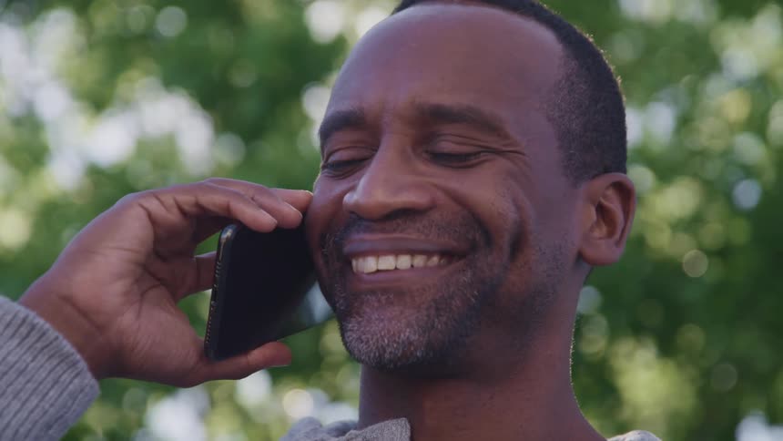 A man laughs while talking on his smartphone outdoors