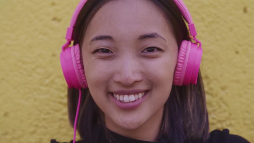 A woman with headphones staring and smiling with a wall in the background
