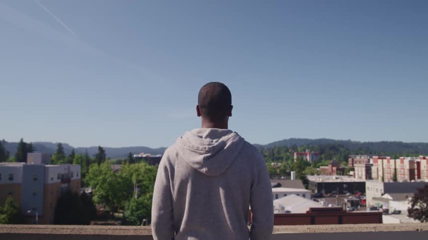 A man standing on a rooftop overlooking a small town
