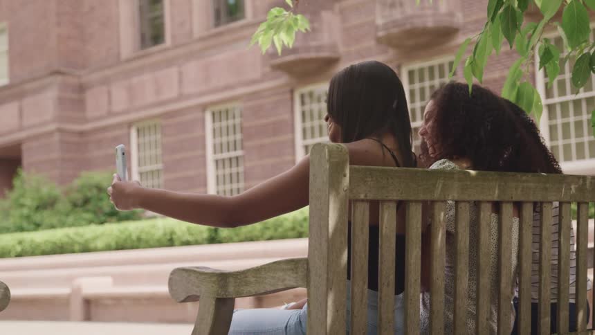 Three female friends smiling while taking a selfie on an outdoor bench