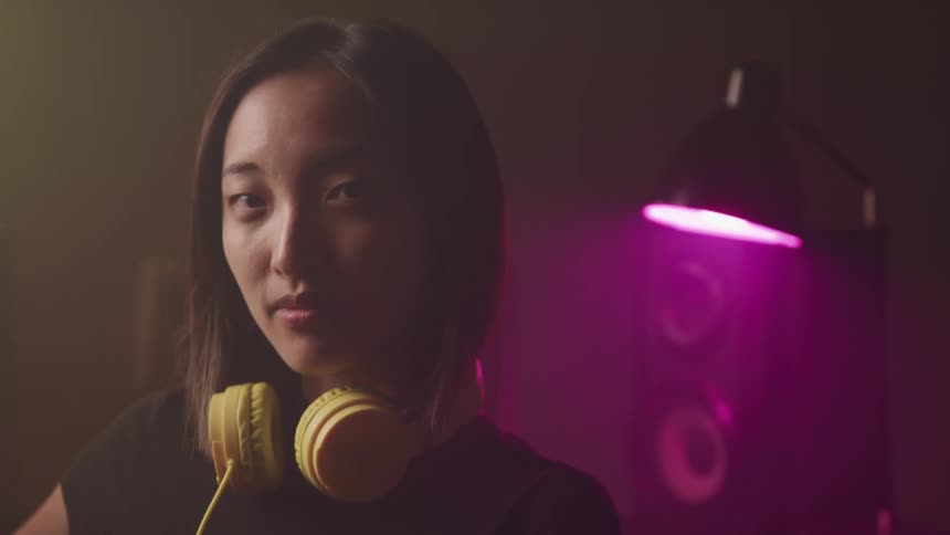 Young woman wearing yellow headphones on her neck looks at the camera