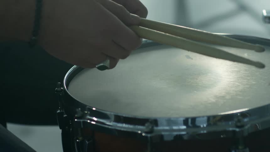 A musician picking up drumsticks from the top of a drum