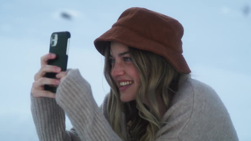 Young woman takes pictures with her smartphone in the mountains at winter