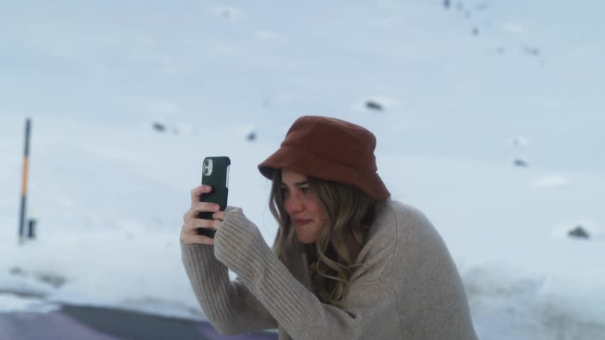 Young woman taking pictures with her phone on the mountain at winter