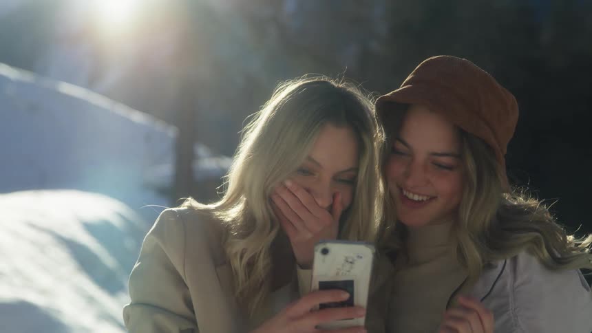 Two woman standing and laughing while looking at a smartphone