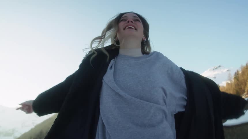 Woman smiles and laughs as she spins outdoors with snow covered forest and mountains in background