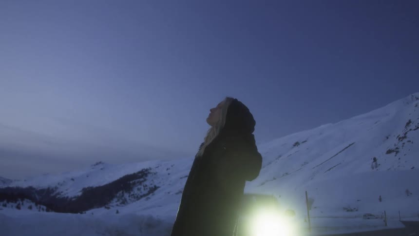 A woman standing with a vehicle a mountain range the sky and clouds in the background
