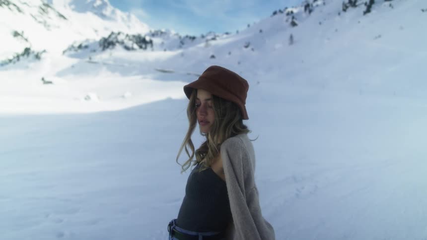 Young woman wearnig a hat and a coat modeling on the snow covered slopes of a mountain