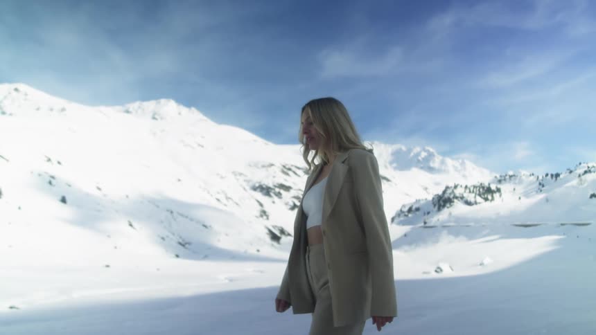 A woman in a suit walks through a frozen mountain landscape on a clear day