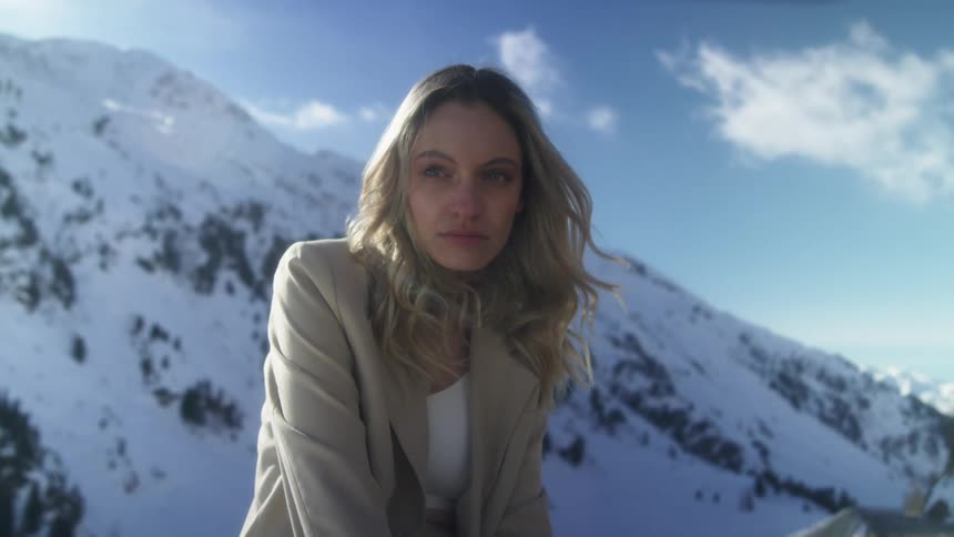 A woman with a jacket with a mountain range the sky and clouds in the background