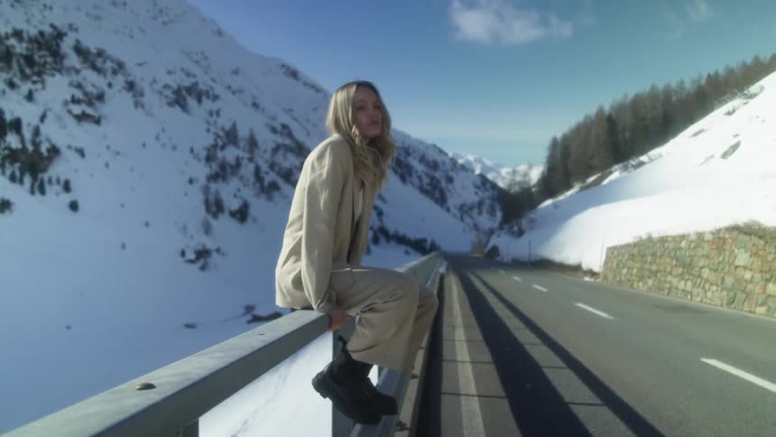 A woman sitting on railing on the side of a mountain road in winter