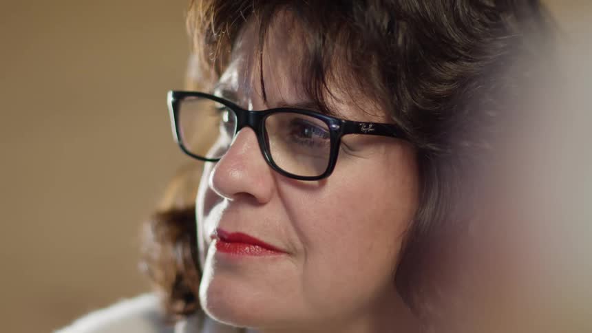 Middle aged woman with brown hair and glasses looks sideways