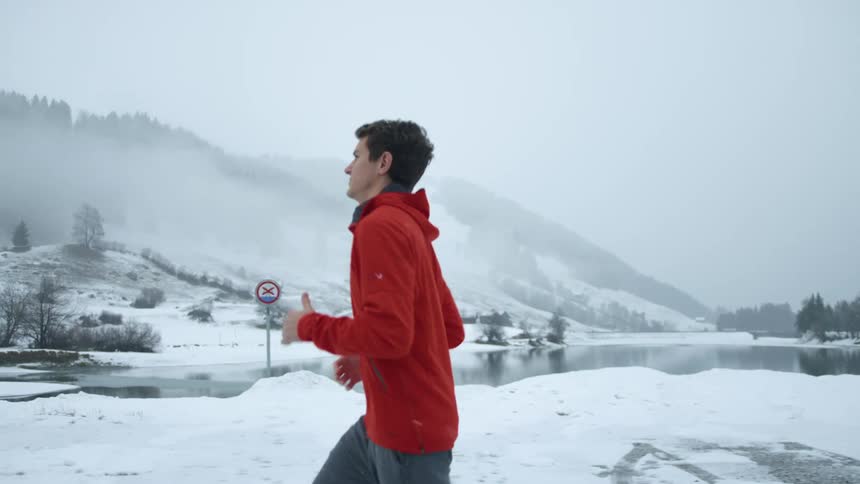 A man jogging with trees a snow covered mountain range the sky and clouds in the background