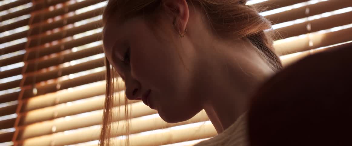 A woman with a sweater in a room with a window and blinds in the background