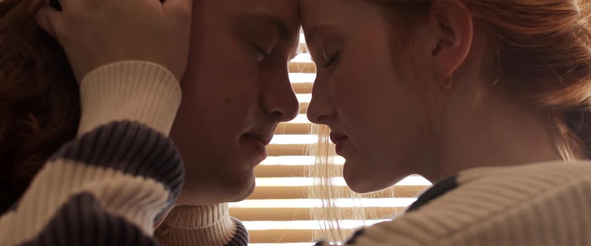 A young woman holds her husbands head as they embrace and cry while standing in front of a window