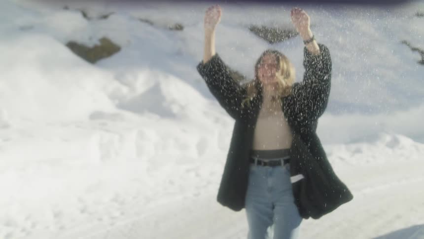 A teenage girl laughs as she throws snow in the air