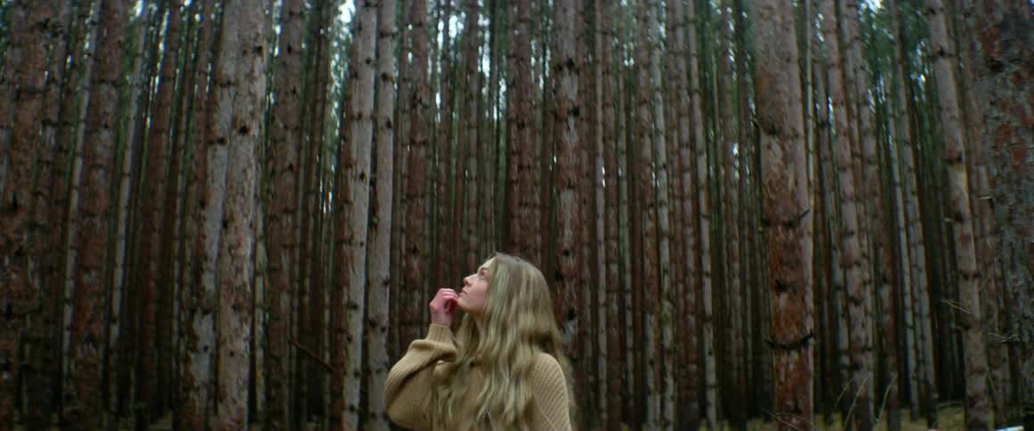 Blonde woman with a beige pullover looks around in the woods