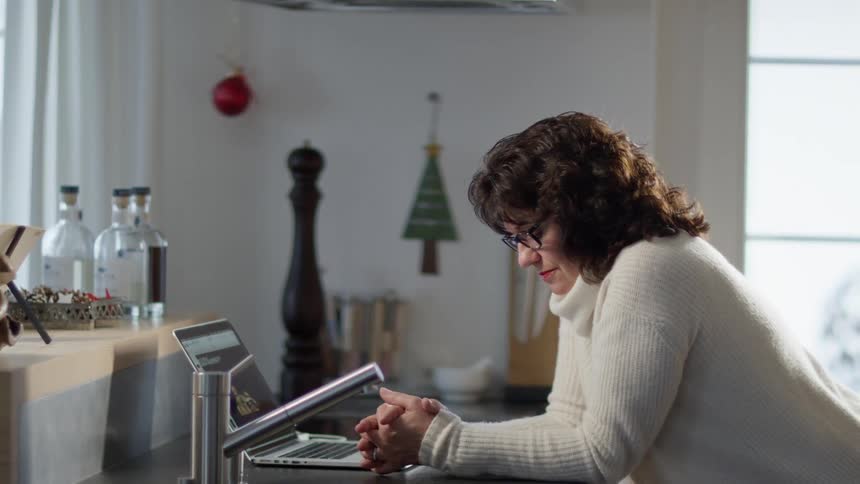 Tired woman reclined on the kitchen counter top next to a laptop