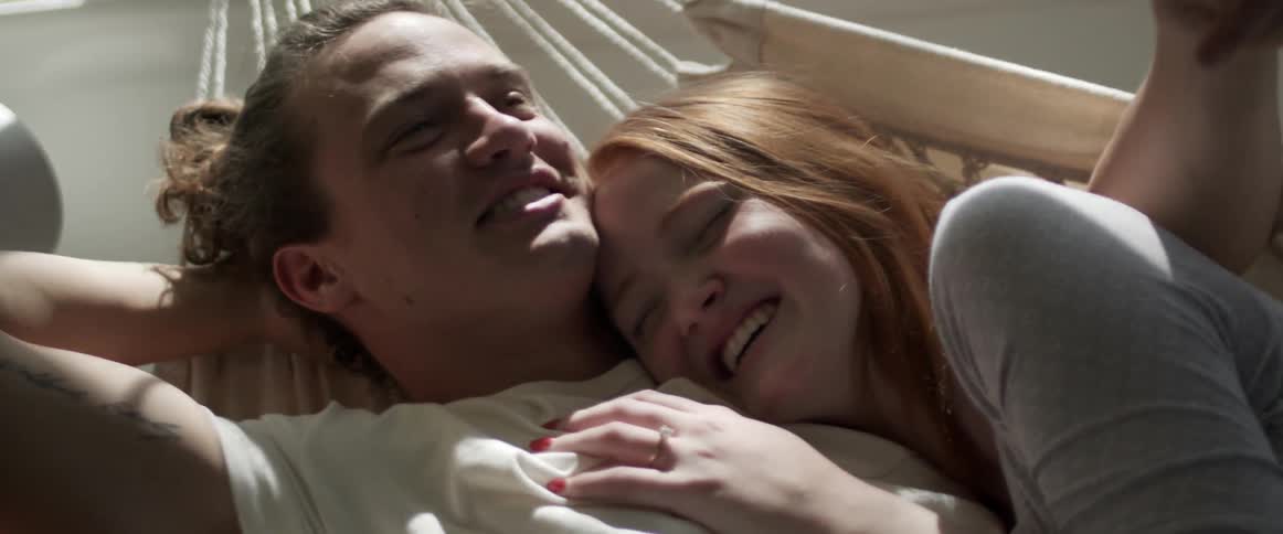 Couple lies in hammock cuddling as they laugh and talk